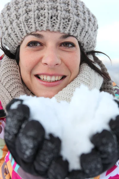 Mulher todos os sorrisos na estância de esqui com neve nas mãos — Fotografia de Stock
