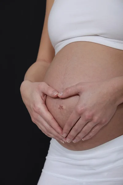Žena tvoří srdce s rukama na její těhotné břicho — Stock fotografie