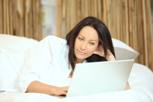 Femme avec un ordinateur portable sur son lit — Photo
