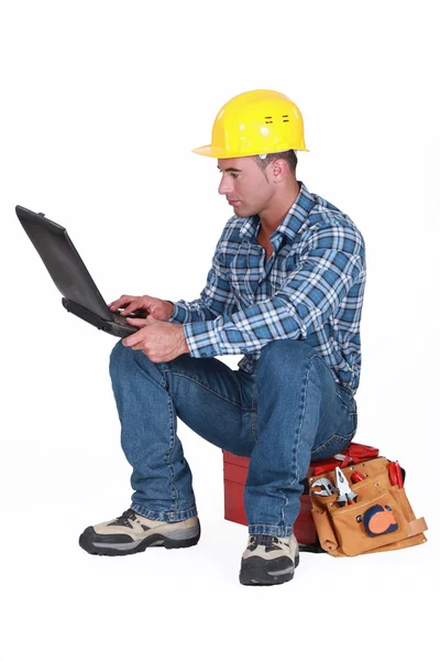 Trabalhador sentado em uma caixa de ferramentas com notebook — Fotografia de Stock