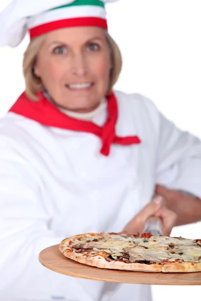 55 ετών γυναίκα πίτσα μαγειρέψουν χρησιμοποιώντας ένα φτυάρι και φοράει ομοιόμορφη πίτσα μάγειρας — Φωτογραφία Αρχείου
