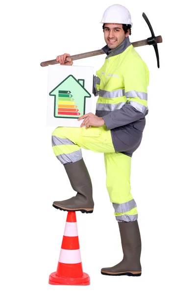 Obrero de la construcción sosteniendo un pico y una señal de eficiencia energética — Foto de Stock