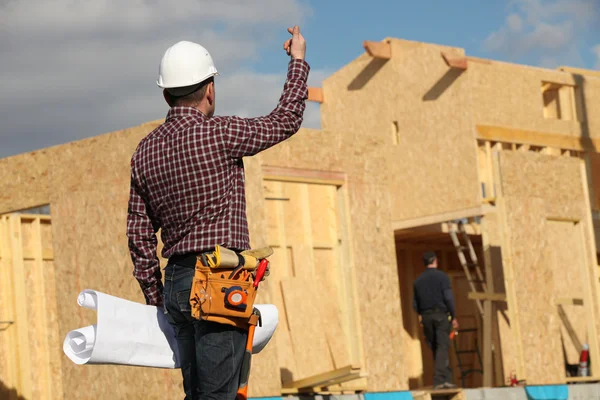 Handwerker steht vor einem unfertigen Haus — Stockfoto