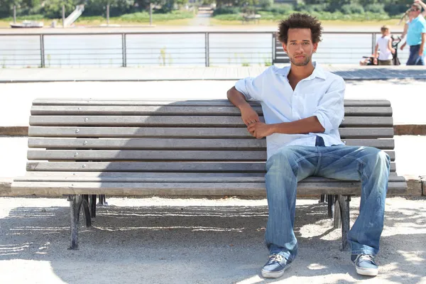 Молодий чоловік сидить на громадській лавці — стокове фото