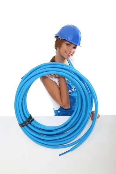 Portrait of cute female plumber carrying hose with copyspace against studio background — Stock Photo, Image