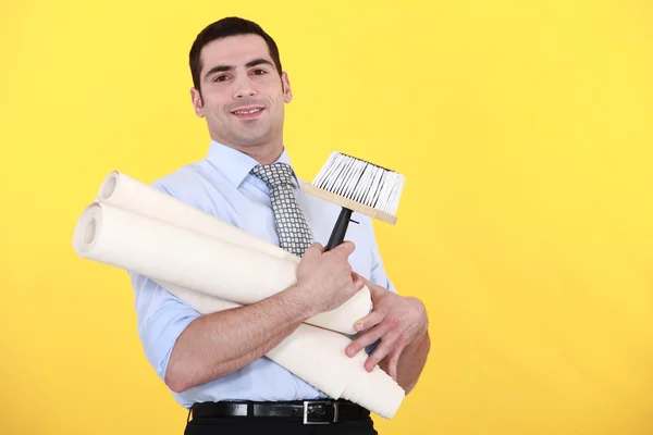 Jovem homem bonito carregando rolos de papel de parede contra fundo amarelo — Fotografia de Stock