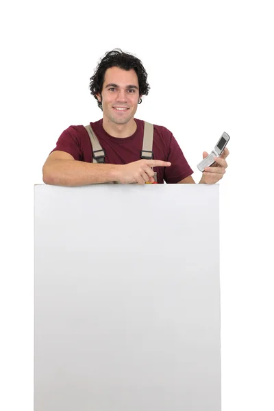 Handyman com um celular e uma placa deixou em branco para sua mensagem — Fotografia de Stock
