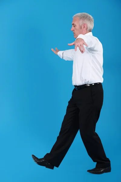 Senior businessman pretending to walk on wire — Stockfoto