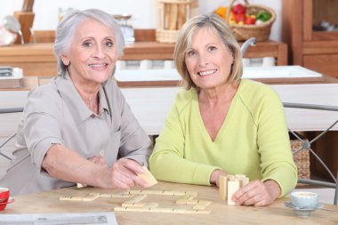 Duo of retired ladies playing scrabble in the kitchen clipart