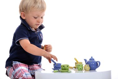 Little boy playing with a doll's tea set clipart