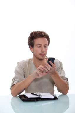 Man texting on his cellphone with an open diary on a white desk clipart