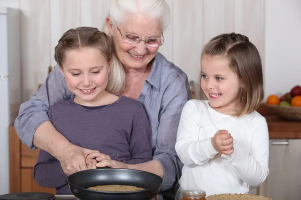 Sisters cooking pancakes with grandmother — Stock Photo, Image