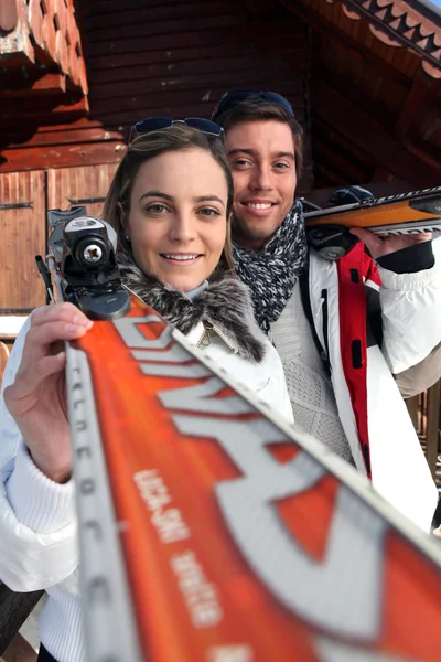 Couple stood by chalet with skis — Stock Photo, Image