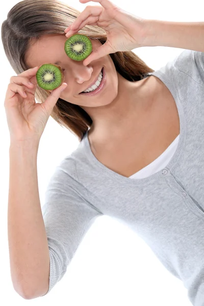 Молодая женщина улыбается, скрывая глаза киви-фруктами — стоковое фото