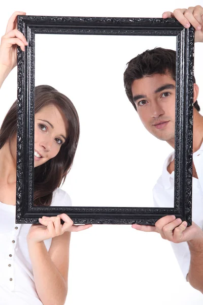 Man and woman holding up a picture frame — Stock Photo, Image