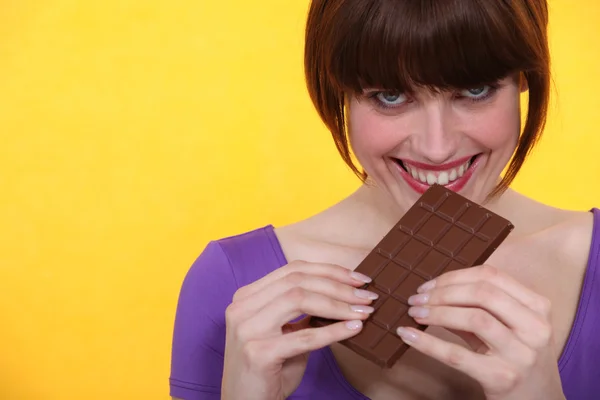 年轻女子沾沾自喜于巧克力棒黄色背景 — 图库照片