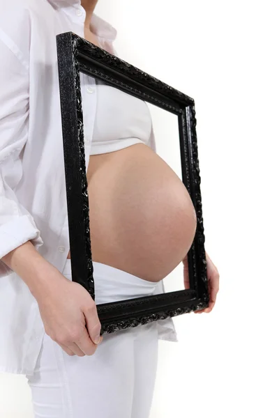 Беременная женщина протыкает живот рамкой — стоковое фото