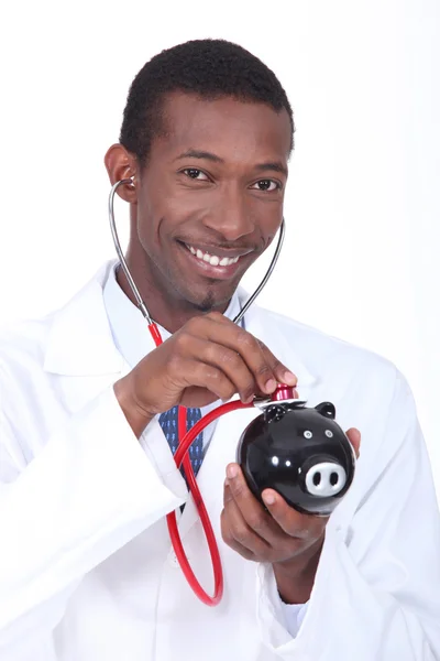 Человек, использующий стетоскоп, чтобы проверить здоровье копилки — стоковое фото