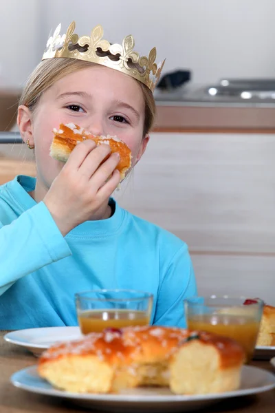 Lilla flickan äta kakan samtidigt som bär en krona — Stockfoto