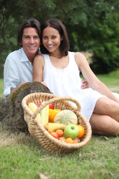 Pareja sentada en la hierba con cesta de frutas —  Fotos de Stock