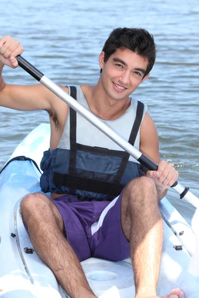 Rapaz de cabelos escuros remando em uma canoa — Fotografia de Stock
