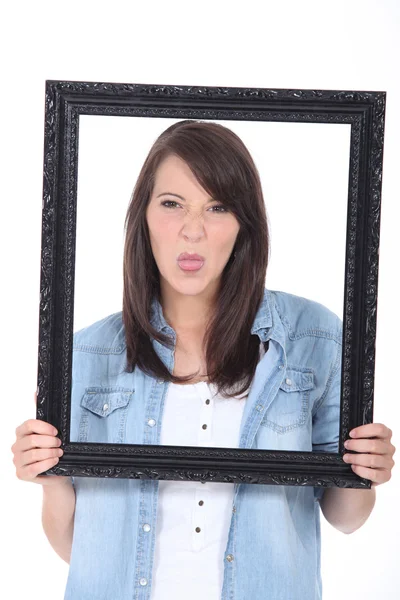 Mujer joven sosteniendo un marco de imagen y sacando la lengua —  Fotos de Stock
