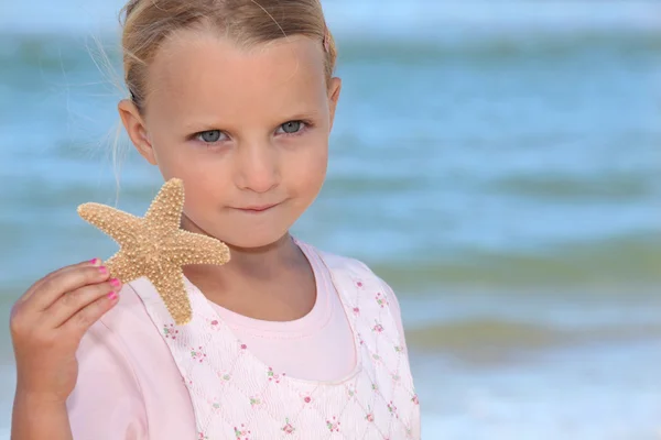 Cute little girl holding starfish against sea background — Stock Photo, Image
