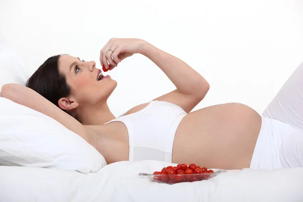 Schwangere isst Kirschtomaten im Bett — Stockfoto