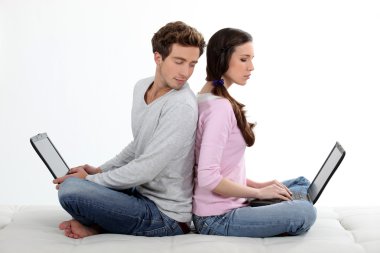 Portrait of lovely young couple back-to-back with laptop clipart