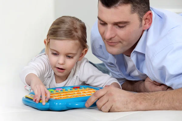 Отец смотрит, как дочь играет с электронной игрушкой — стоковое фото