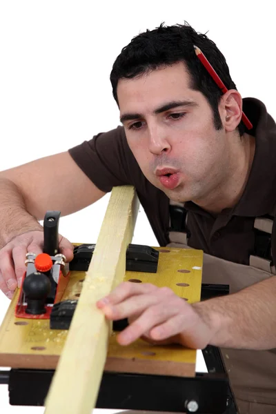 Tradesman blowing shavings off of a wooden plank — Stock Photo, Image
