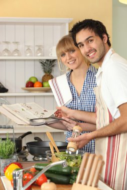 Couple preparing a meal with the help of a cookbook clipart