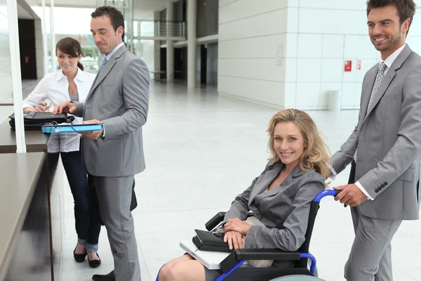 Επιχειρηματίας σε μια αναπηρική καρέκλα με τους συναδέλφους check-in στη ρεσεψιόν — Φωτογραφία Αρχείου