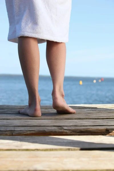 Woman in a toweling robe standing barefoot on a wooden jetty — Stock Photo, Image