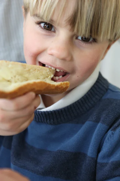 Little blond boy eating slice of bread and butter — Stock Photo, Image