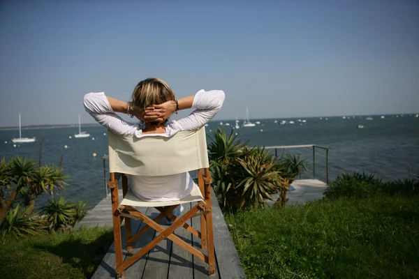 Woman sitting in a chair by the waterfont — Stock Photo, Image