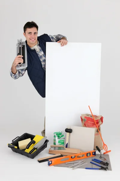 Fliesenleger steht hinter seinen Werkzeugen, Baumaterialien und einem leeren Schild — Stockfoto