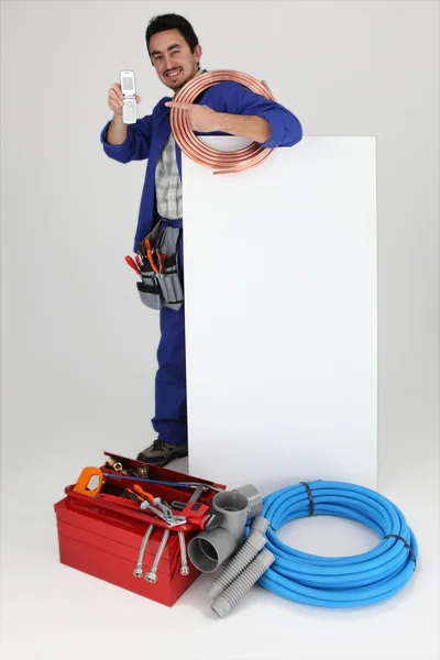 Homem com placa em branco e ferramentas, apontando para o celular — Fotografia de Stock