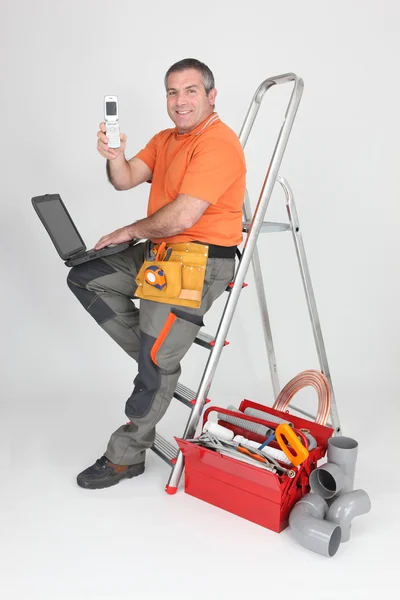 坐在梯子显示手机上的水管工 — 图库照片