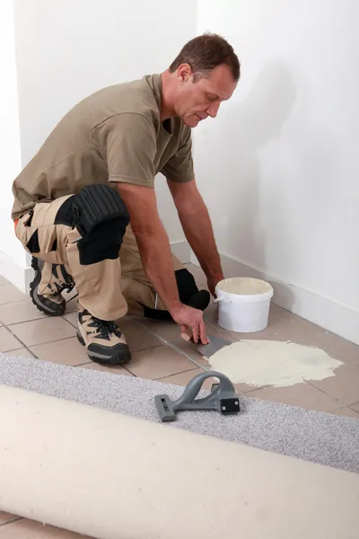 Montador de carpete espalhando adesivo em um piso de azulejos — Fotografia de Stock