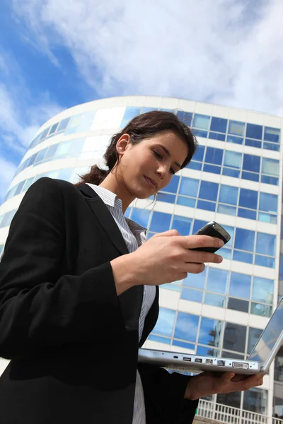 Женщина пишет смс на мобильном телефоне возле офисного здания — стоковое фото