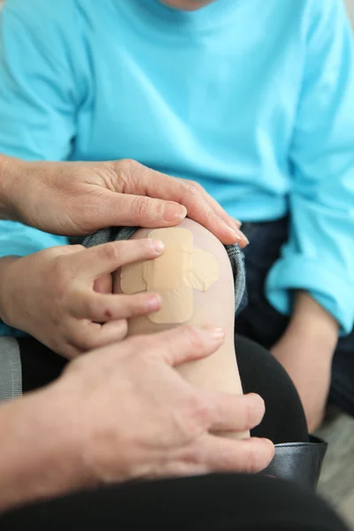 An adult putting a plaster on a child's knee — Stock Photo, Image