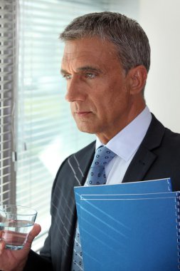 Mature businessman standing close to the window clipart