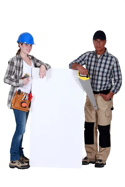 Ремесленница и мастер позируют рядом с пустым плакатом — стоковое фото