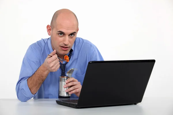 Člověk jíst z cínu před jeho laptop — Stock fotografie