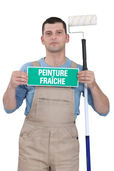 Painter holding fresh paint sign and roller — Stockfoto