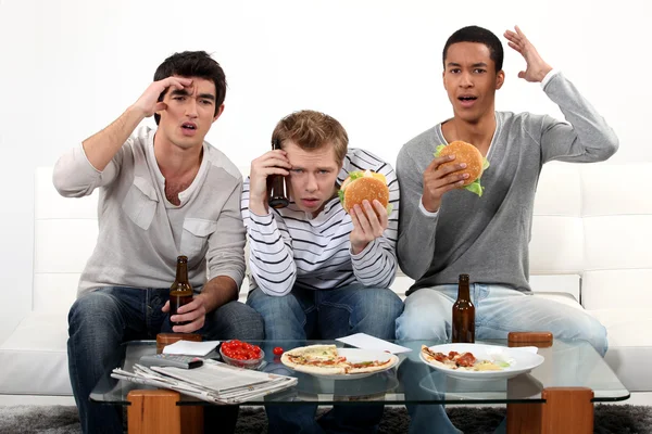 Three young eating burgers and drinking beer — Stock Photo, Image