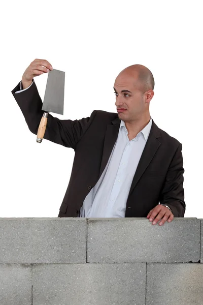 Muž v obleku drží lopatu za cihlová zeď — Stock fotografie