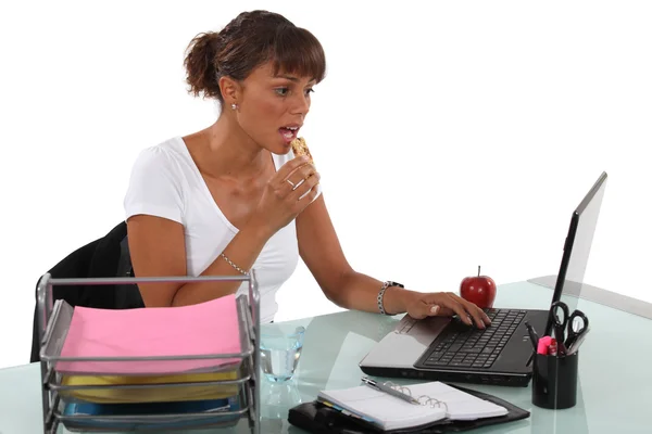 Mujer tomando un aperitivo mientras está sentada en el escritorio —  Fotos de Stock