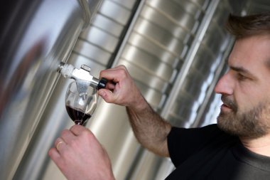 Man sampling red wine from tap clipart
